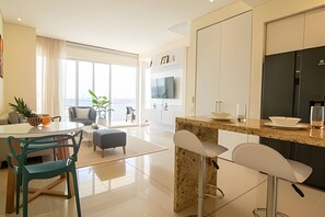 A modern kitchen with a central island, white bar stools, and a dining area with a table and chairs. - Luxurious 1 bedroom apt - 15th floor of h2 (Cartagena)
