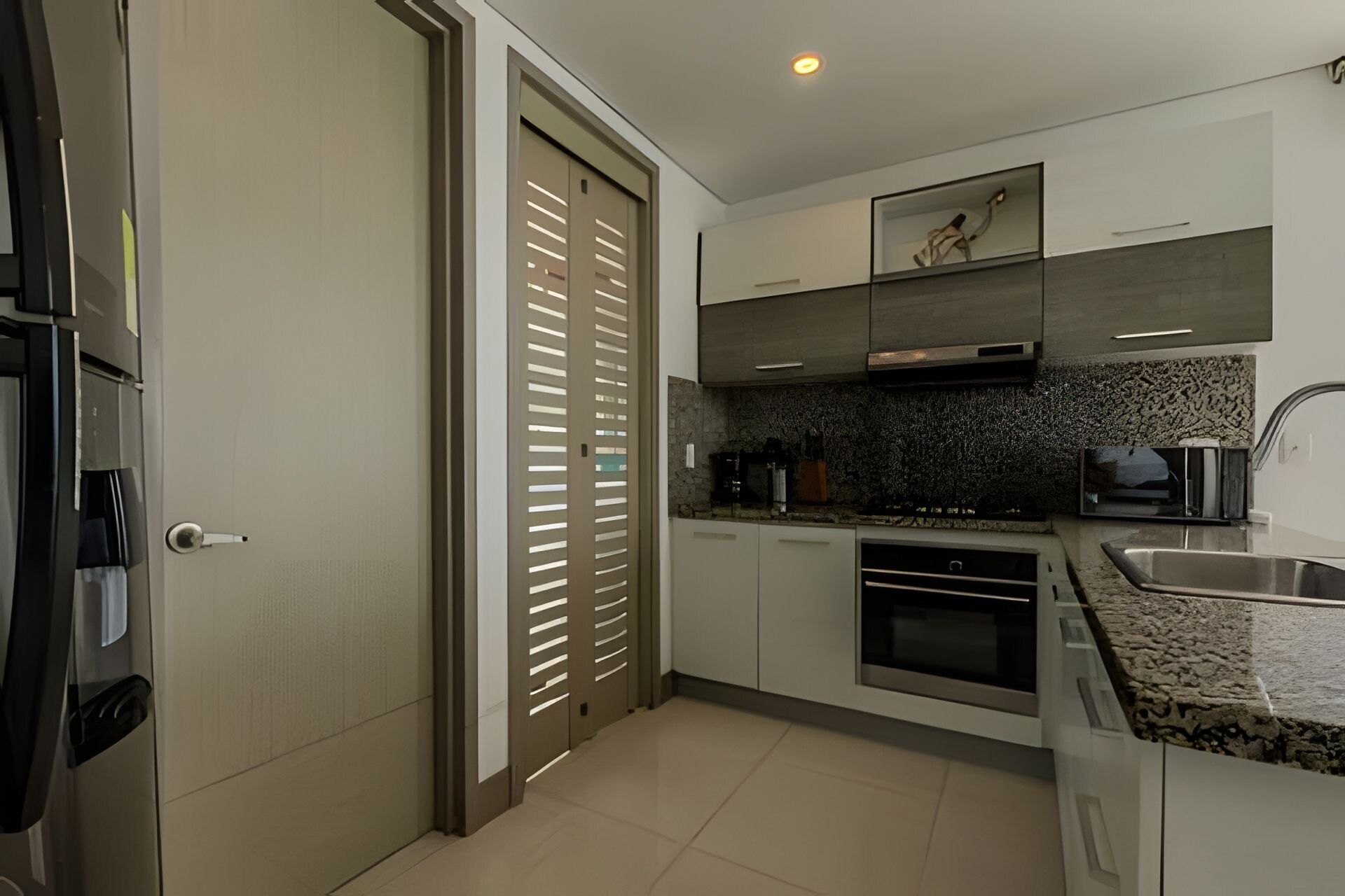 A modern kitchen with a built-in oven, a stainless steel sink, and a granite countertop.