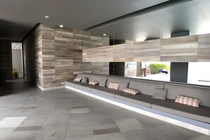 A modern interior with a long bench seating area, a stone wall, and a large window overlooking a street. - Morros City-Spectacular 38th Floor apt Bocagrande (Cartagena)