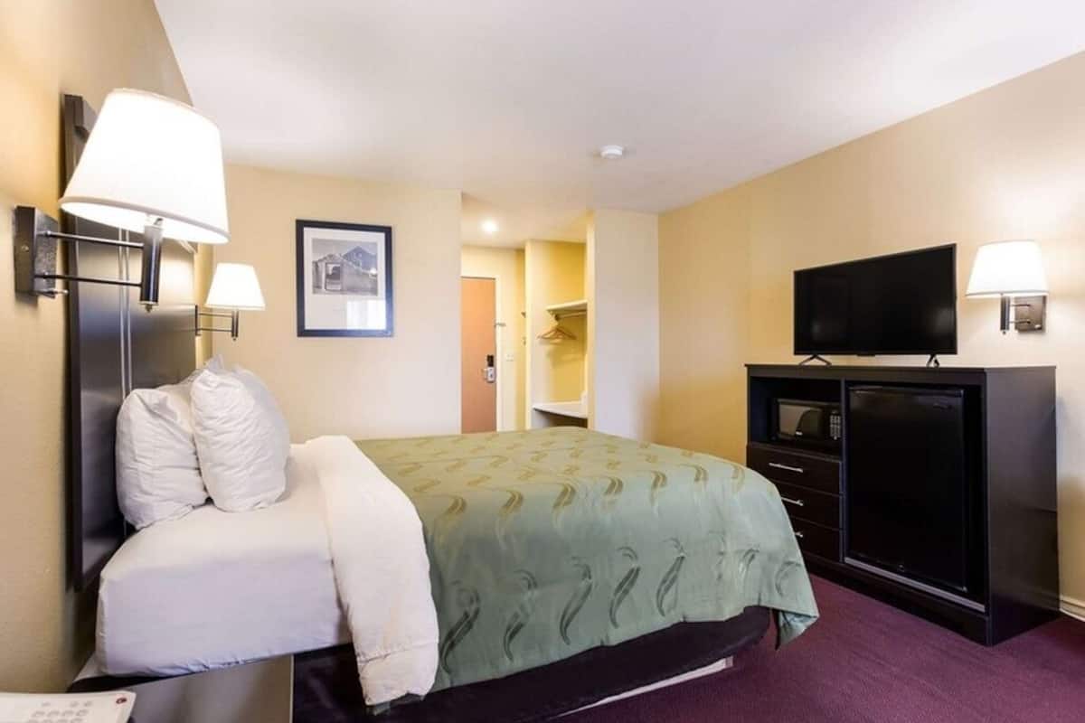 A hotel room with a bed, bedside lamps, a television, a wardrobe, and a framed picture on the wall.