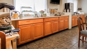A kitchen with wooden cabinets, a breakfast bar, a coffee maker, and a TV mounted on the wall. - Urban Inn & Suites (Boise)