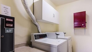 A laundry area with a washing machine, dryer, and a utility cabinet with a sign instructing to use $1 bills only. - Urban Inn & Suites (Boise)
