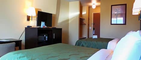 Habitación de hotel con dos camas, un escritorio con computadora, televisión y microondas.