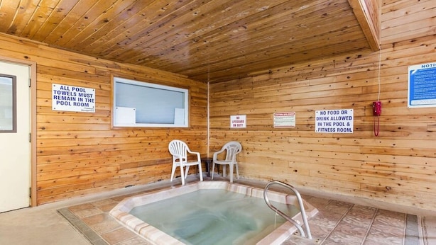 A wooden cabin with a hot tub, two white chairs, and signs indicating pool rules. - Urban Inn & Suites (Boise)