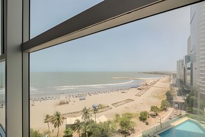 A beach view from a window overlooking a sandy beach with a pool and palm trees. - Spectacular ocean view - Infinito 1002 Building (Cartagena)