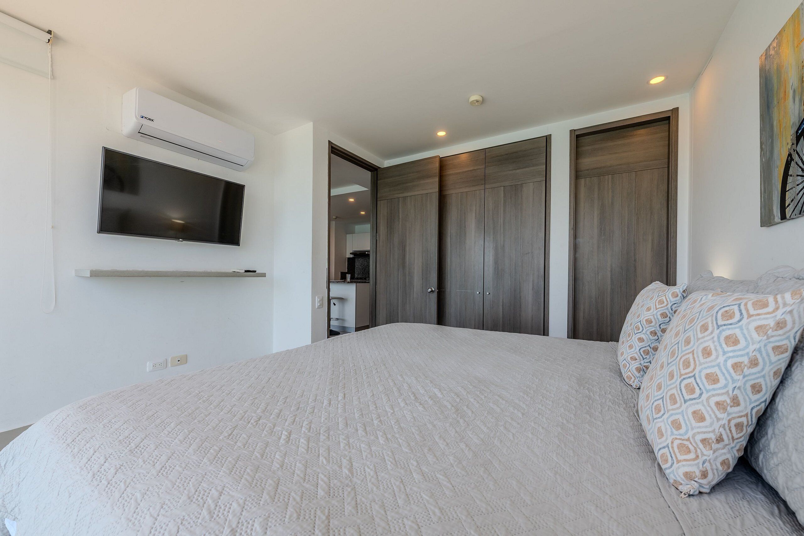 Un dormitorio con una cama grande, televisor montado, equipo de aire acondicionado y un armario con puertas correderas.