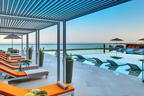 Un espace piscine aménagé sur le toit, avec des chaises longues et des parasols, offrant une vue sur la mer.