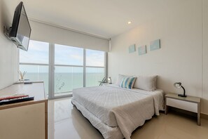 Une chambre avec un lit, un bureau, un téléviseur fixé au mur et une vue sur la mer grâce à de grandes fenêtres.