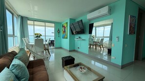 A modern living room with a sofa, coffee table, and a dining area with chairs and a TV. - 29th Floor Spectacular Apt in Palmetto Beach (Cartagena)