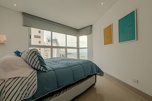 A modern bedroom with a large bed, a view of the city through floor-to-ceiling windows, and two framed artworks on the wall. - Beautiful Apt - 2 Bedrooms 17th Floor Murano Elite (Cartagena)