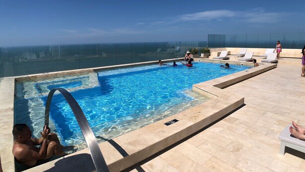 Ein Pool auf dem Dach mit klarem, blauem Wasser, umgeben von Liegestühlen und einer Glasumrandung.