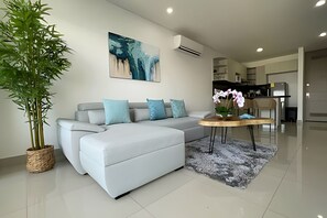 A modern living room with a grey sectional sofa, a round wooden coffee table, and a large potted plant. - Infinitum Spectacular 23rd floor 1 BR Condo (Cartagena)