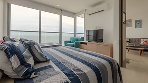 A modern bedroom with a large bed, a TV, and a view of the sky through large windows.