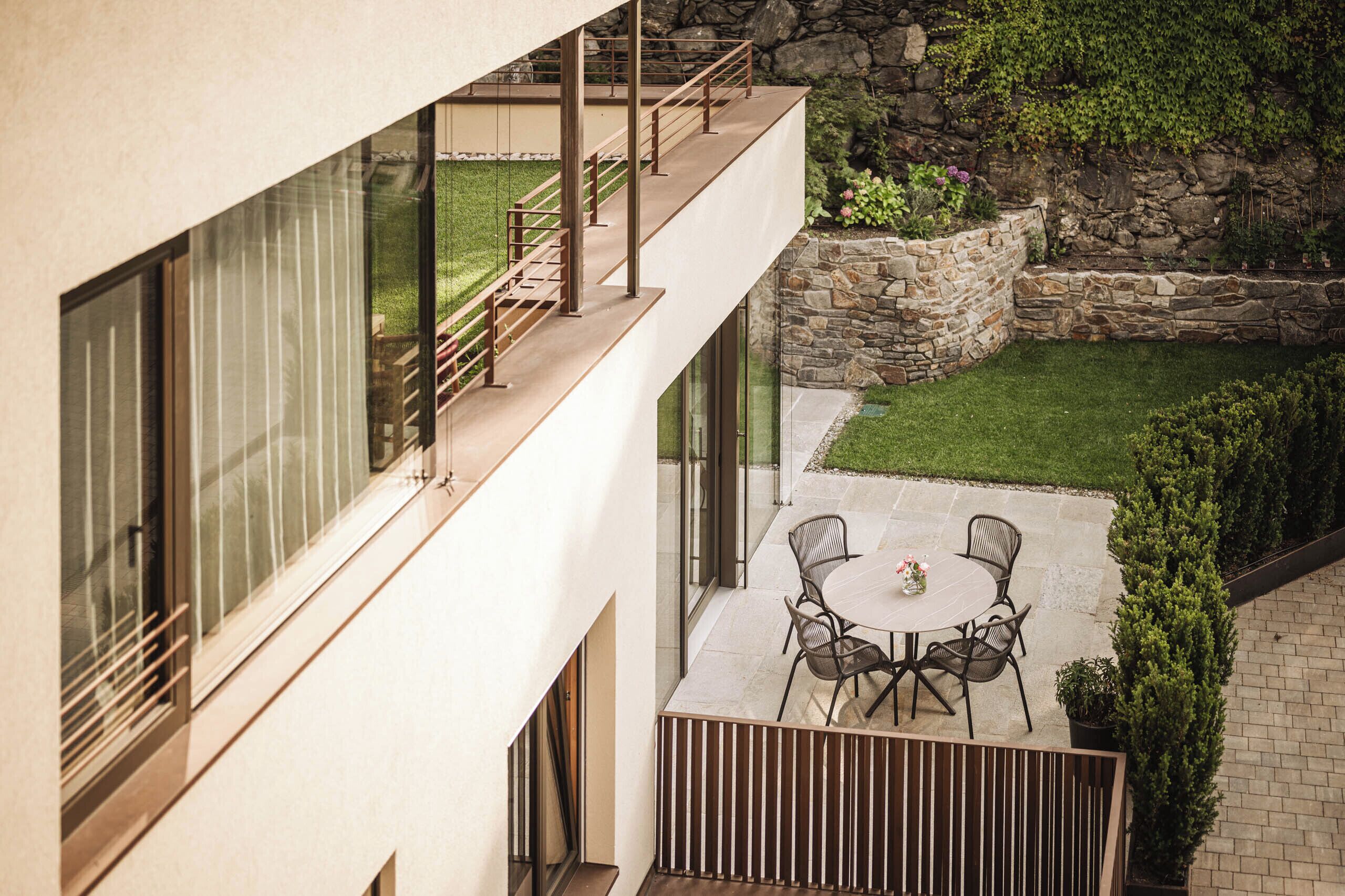 Un bâtiment moderne doté d’un balcon, d’un mur en pierre et d’une pelouse bien entretenue.