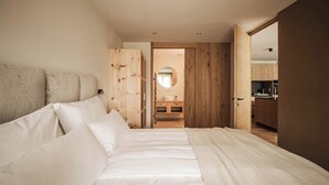 A bedroom with a large bed, wooden wardrobe, and a view into the kitchen. - Garden Apartment Bachquell (Brixen)