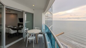 Un balcone con tavolo e sedie, una porta vetrata che dà su una stanza e vista sul mare.