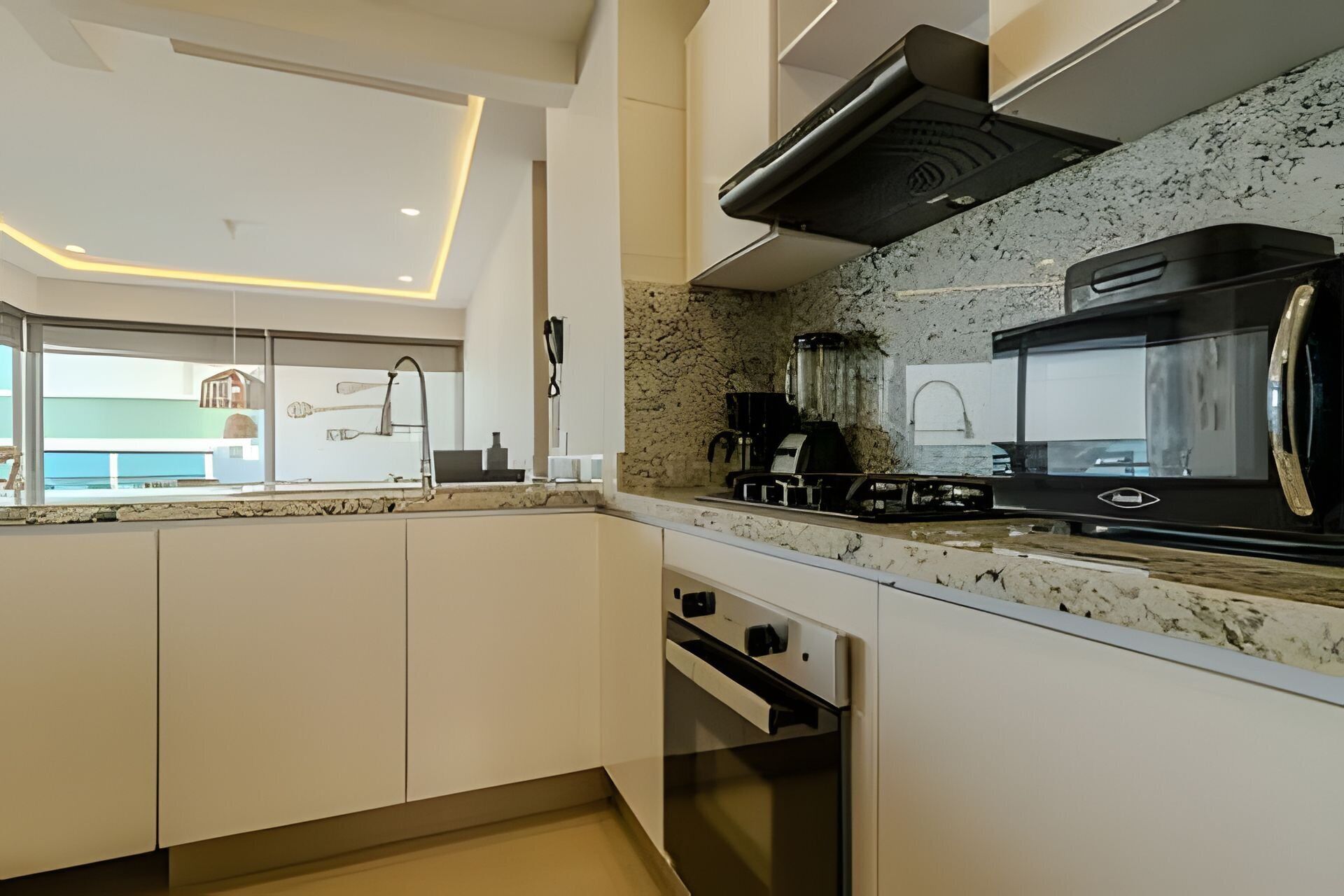 Eine moderne Küche mit weißen Schränken, einer Granit Arbeitsplatte, einem eingebauten Backofen, einer Mikrowelle und einer Kaffeemaschine.