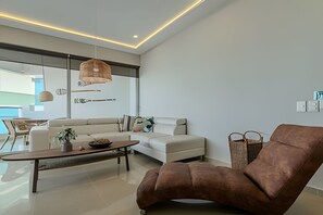 A modern living room with a sofa, a brown armchair, a coffee table, and a hanging light fixture. - Spectacular Ocean View - Infinito 702 Building (Cartagena)