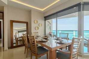 Une salle à manger moderne avec une table en verre, des chaises en bois et une vue sur la mer.