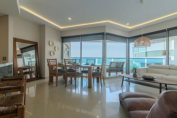 Un salon moderne avec un coin repas, de grandes fenêtres et une vue sur la mer.