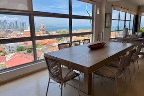 A dining area with a large window overlooking a cityscape and the sea. - Spectacular 2-bedroom apt in the Historic Center (Cartagena)