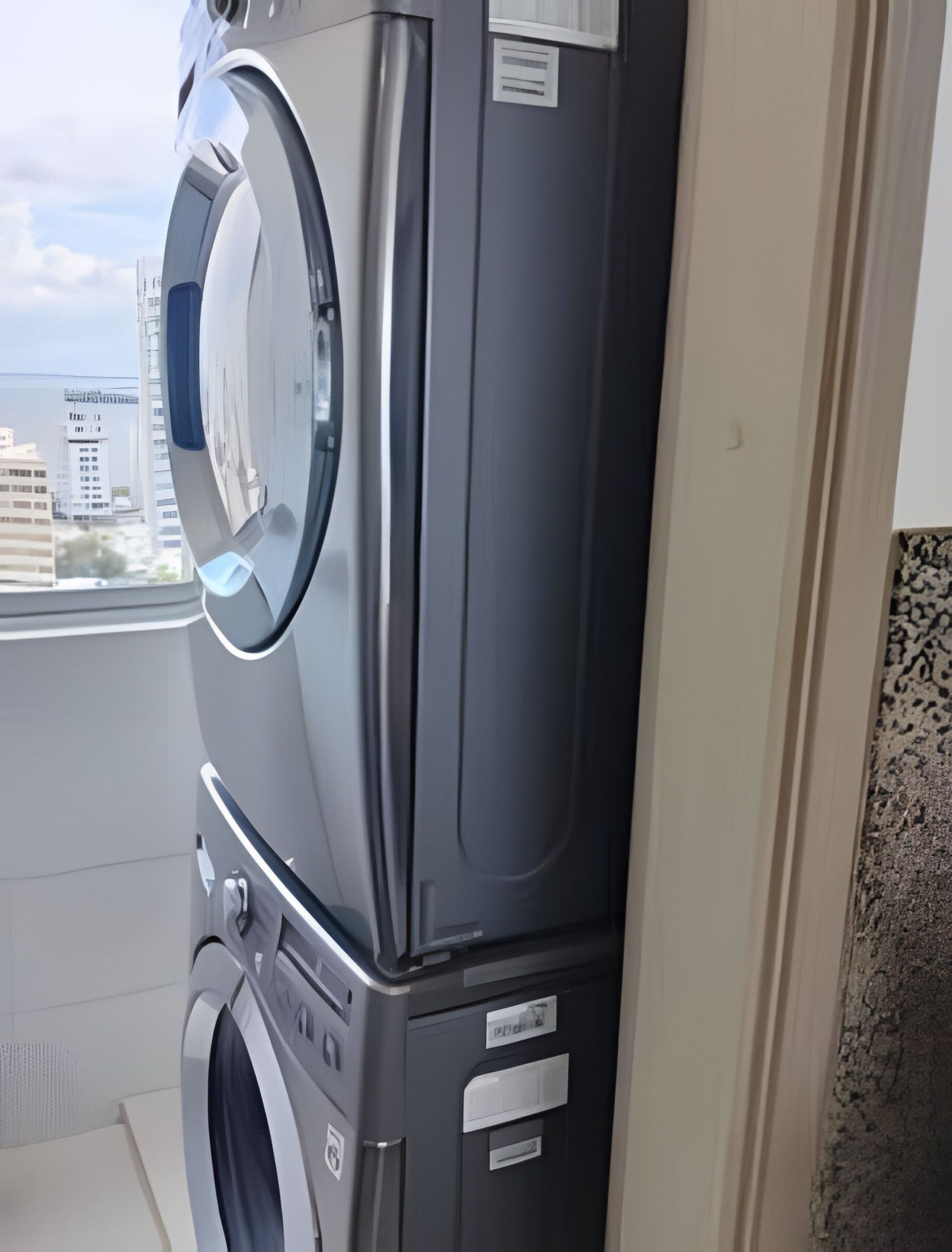 A compact, modern laundry room with a front-loading washer and dryer, a small window with a view of buildings, and a tiled backsplash.