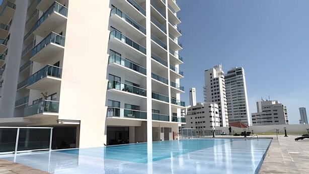 Ein modernes Gebäude mit Schwimmbad, mehreren Balkonen und blauem Himmel.