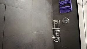 Ein Duschbereich mit einer gefliesten Wand, einem Metallregal und einem violetten Stauraum.