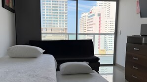 Ein Schlafzimmer mit großem Fenster, einem Bett, einem Schminktisch und einem schwarzen Sofa.