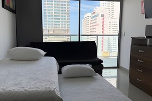 A bedroom with a large window, a bed, a dresser, and a black sofa. - Beautiful 1 Bedroom Ocean View Apartment - 10th Floor (Cartagena)