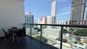 Ein Balkon mit Tisch und Stühlen, der einen Blick auf eine Stadtlandschaft mit verschiedenen Gebäuden bietet.