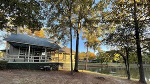 A lakeside building with a covered porch and picnic tables. - Couples Retreat with King Canopy Bed, Jacuzzi for Two, Fireplace & Pond-View Porch (Zwolle)