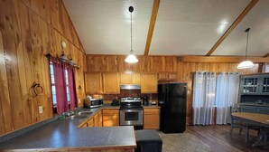 A wooden kitchen with a central island, stainless steel appliances, and a dining area with a table and chairs. - Couples Retreat with King Canopy Bed, Jacuzzi for Two, Fireplace & Pond-View Porch (Zwolle)