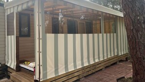 A small, single-story cabin with a wooden exterior and a striped awning. - Mobile home 200 m from the beach in a friendly, wooded 3* campsite. (Saint-Georges-de-Didonne)