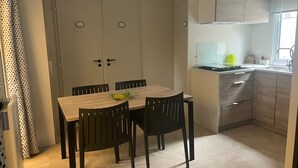 A compact kitchen with a dining area, featuring a wooden table and chairs, a built-in stove, and light-colored cabinets. - Mobile home 200 m from the beach in a friendly, wooded 3* campsite. (Saint-Georges-de-Didonne)