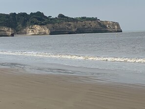 Uma praia com um penhasco rochoso ao fundo.