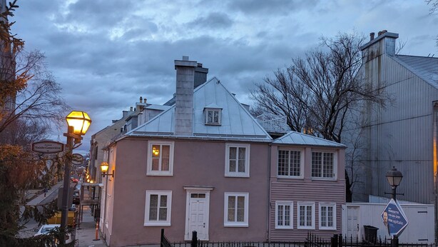 Un bâtiment à deux étages, doté d’une porte blanche et de nombreuses fenêtres, situé dans une rue bordée d’une clôture en métal et d’un lampadaire.