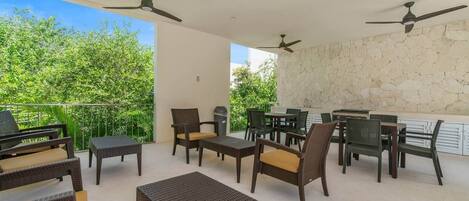 An outdoor patio with wicker furniture, ceiling fans, and a stone wall.