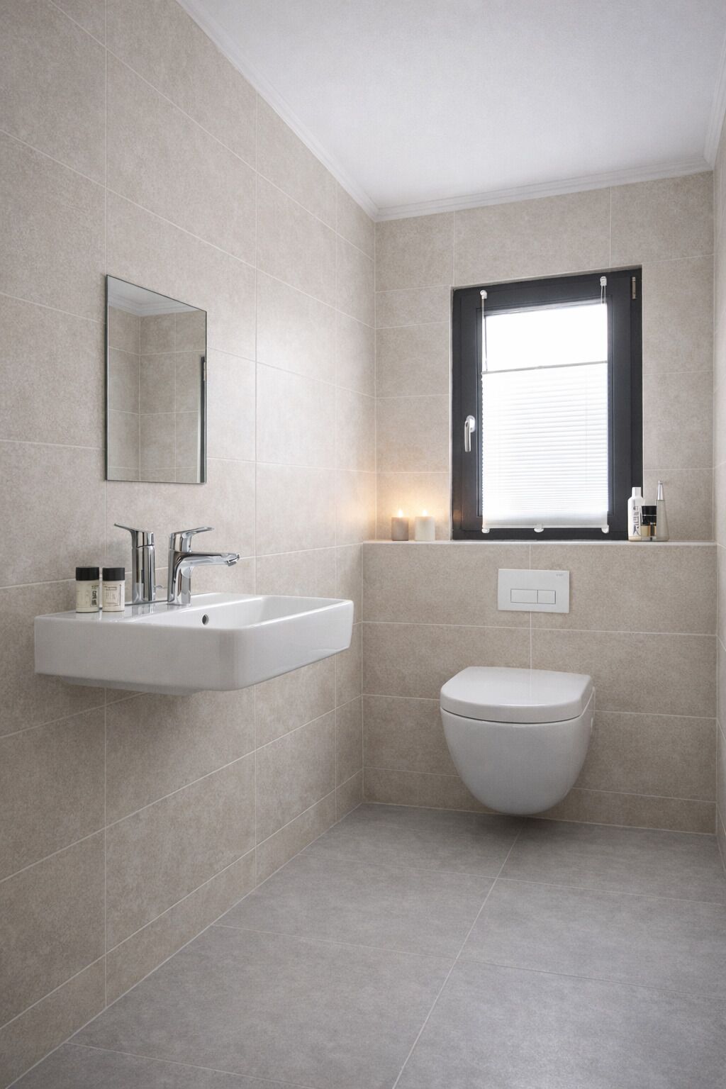 Ein modernes Badezimmer mit einem weißen Waschbecken, einer Toilette und einem Fenster mit Jalousien.