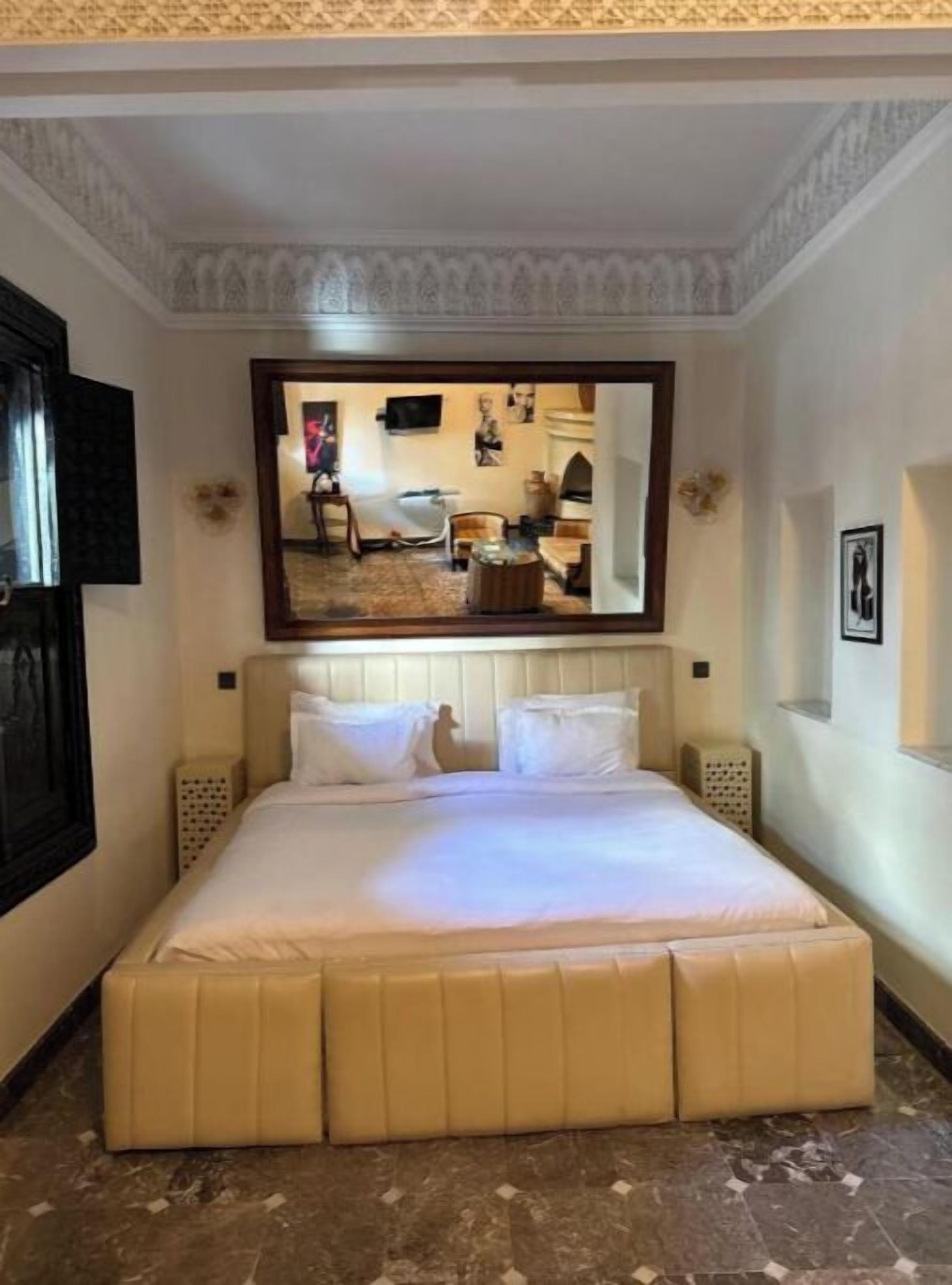 A hotel room with a large bed, a mirror above it, and a small seating area with a table and chairs.