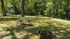 Ein Picknicktisch und eine Feuerstelle in einer bewaldeten Parkanlage.