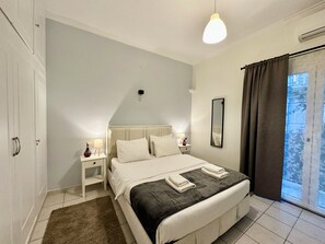 Un dormitorio con cama, mesitas de noche, espejo y vista al exterior a través de una ventana con cortinas.