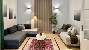 En moderne stue med en sofa, en mindre sofa, et rundt sofabord og en dekorativ plante.