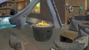 Un área junto a la piscina con tobogán, una fogata y mobiliario exterior.