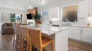 Una cocina moderna con armarios blancos, una isla central y un comedor con sillas de mimbre.