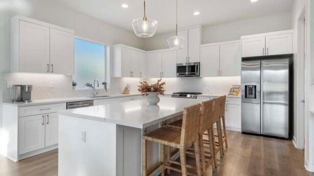Una cocina moderna con armarios blancos, electrodomésticos de acero inoxidable y una isla central con taburetes de bar.