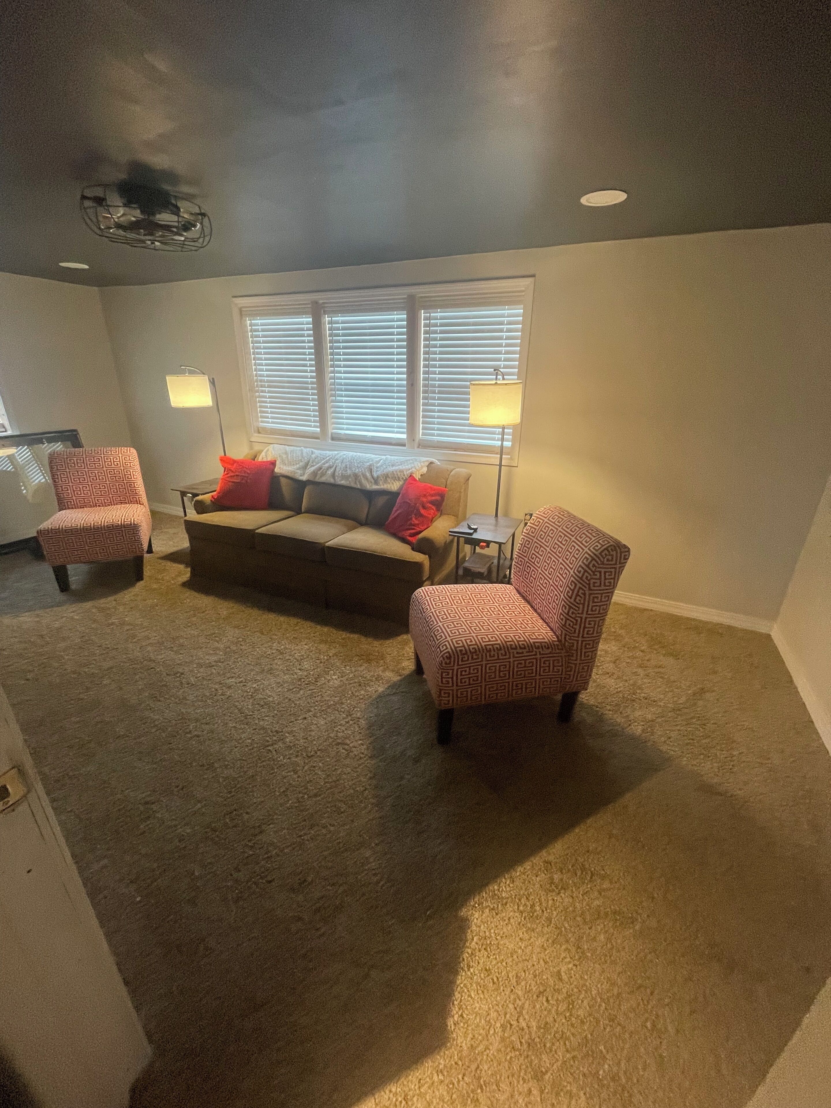 A cozy living room with a sofa, two patterned armchairs, a coffee table, and a floor lamp.