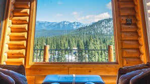 A log cabin interior with a large window offering a mountain view. - Miracle Lodge - Hot Tub, Golf & Mountain Views (Leavenworth)