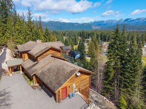 A log cabin hotel with multiple cabins, surrounded by dense forest and mountains in the background.