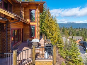 A log cabin with a balcony, a table, chairs, and a view of a forest and mountains.